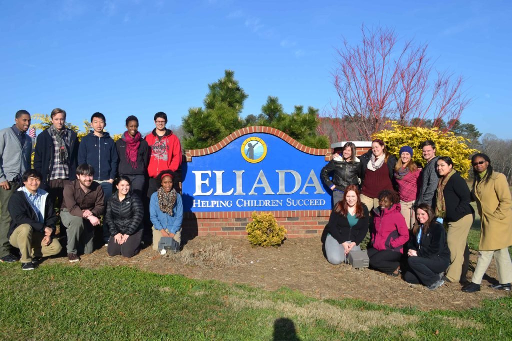A group of staff and young people gathered around the Eliada sign on its campus